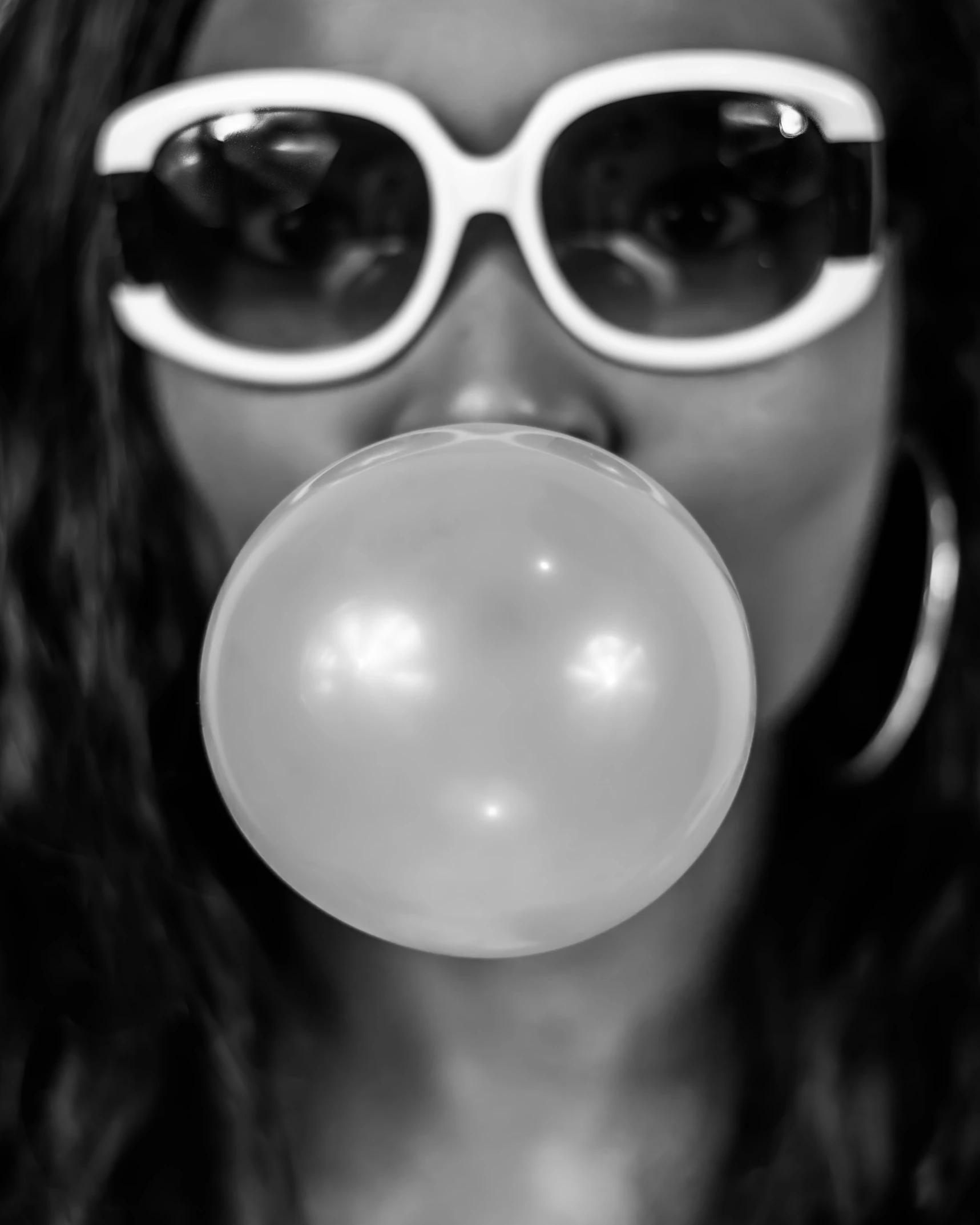 a woman wearing round sunglasses blowing bubbles from her nose