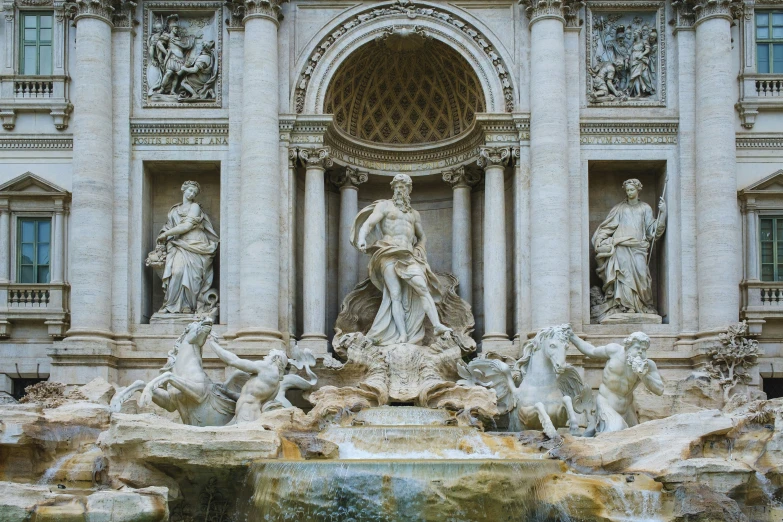 a fountain of many statues in front of a stone building