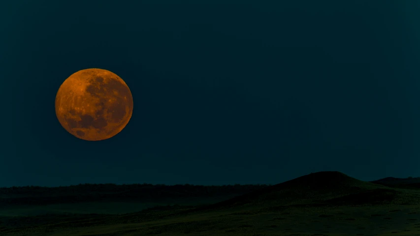 the large orange moon is shining on the blue sky