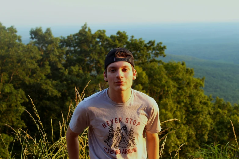 a young man standing in a green forest in front of the mountains