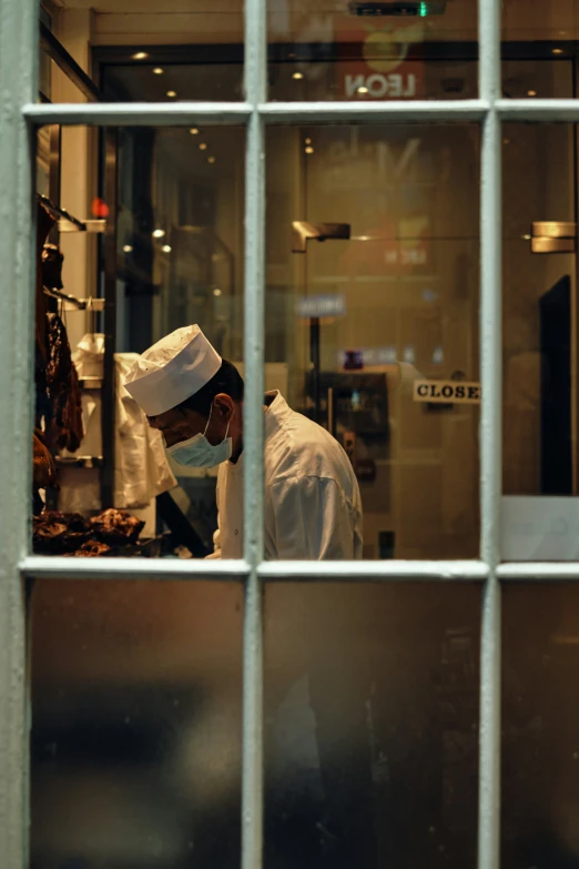 a chef in a white uniform behind glass