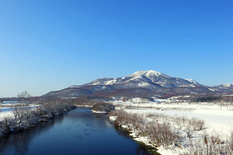 a wide river flowing through a snowy field under a blue sky