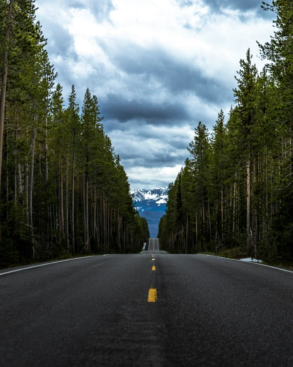 a dark road that leads to a snow capped mountain