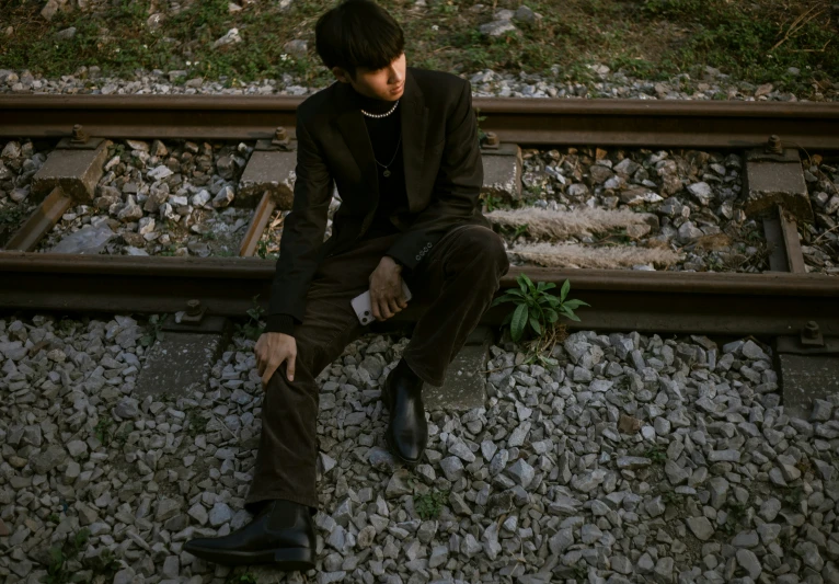 a man sitting on top of train tracks next to rocks