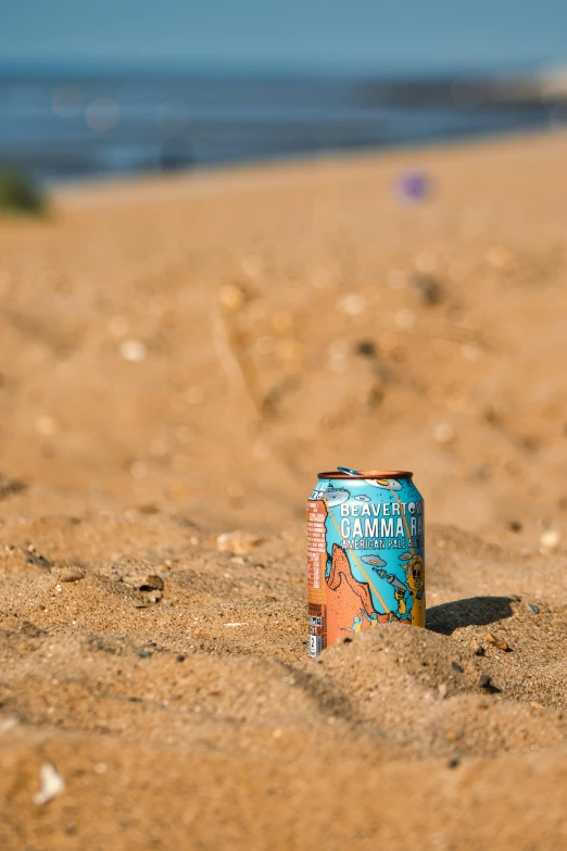 a can of beer sits in the sand next to a beach