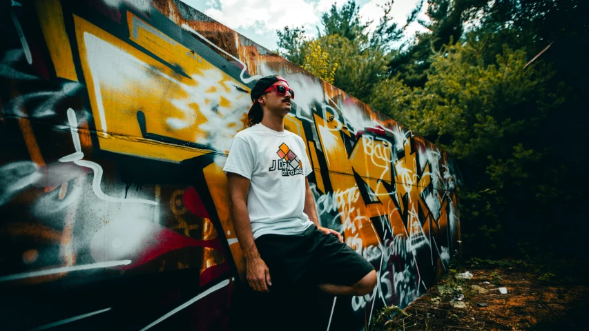 a young man with a white shirt standing next to some graffiti