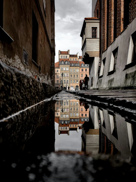 two people standing on a ledge by the water in a narrow city street