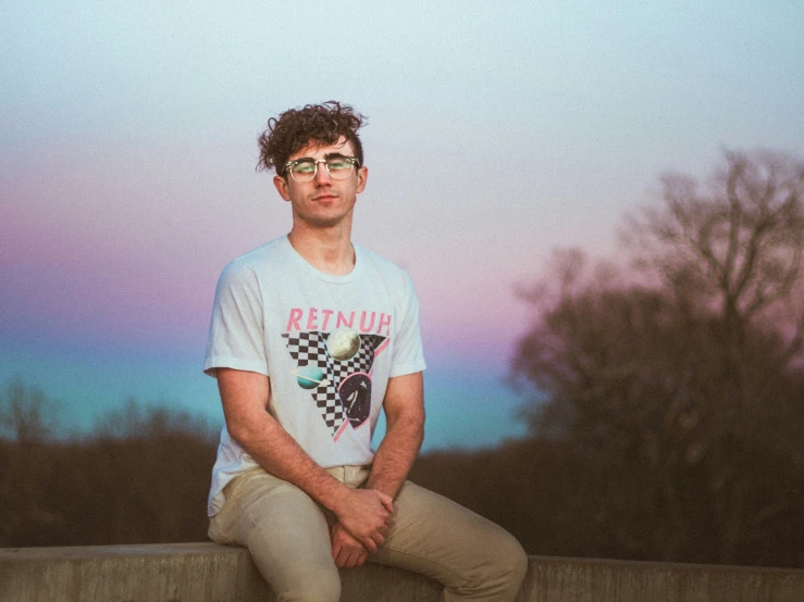 a man sitting on a wall and wearing glasses