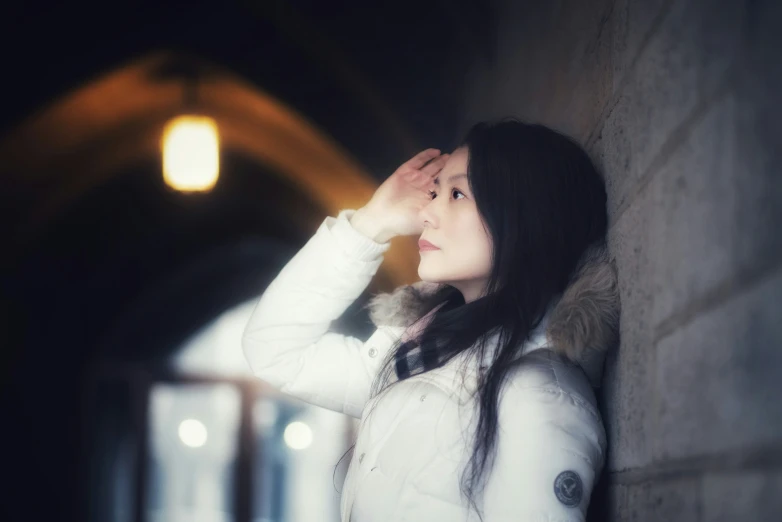 a woman leaning against a stone wall and covering her face with her hands