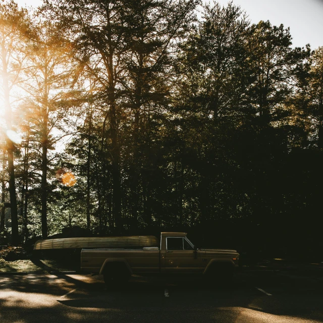 a truck sits in the sun beside some trees