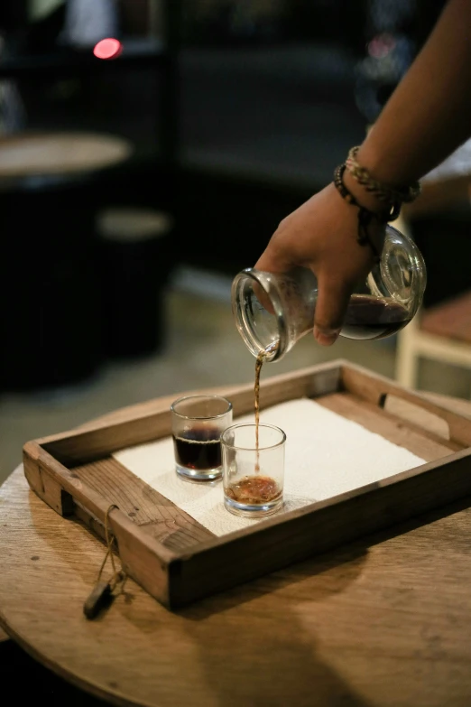 someone pouring coffee into a small glass in a wooden tray