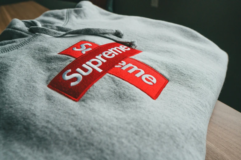 a grey sweatshirt that has a red ribbon that reads supreme