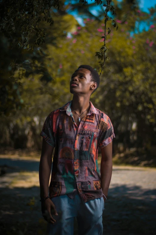 a black man wearing colorful shirt standing by trees