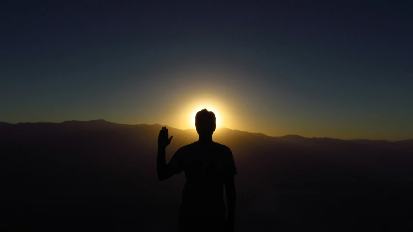 a man silhouetted by the setting sun raising his hand
