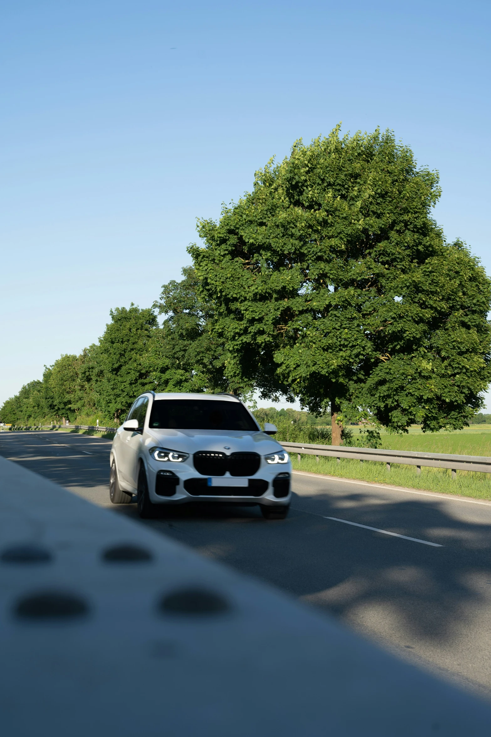 a white bmw suv driving down the road in a forest