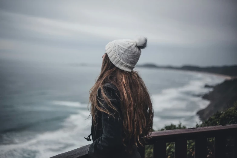 woman with long hair wearing a white hat looking out over the ocean