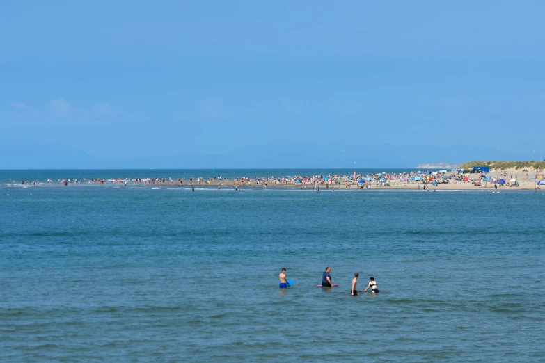 people are wading in the ocean near a crowded beach