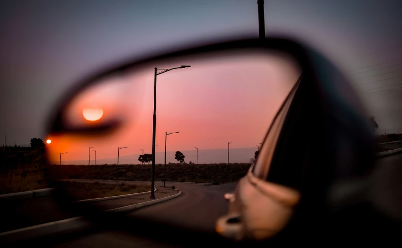 an image of the sun setting in a rear view mirror