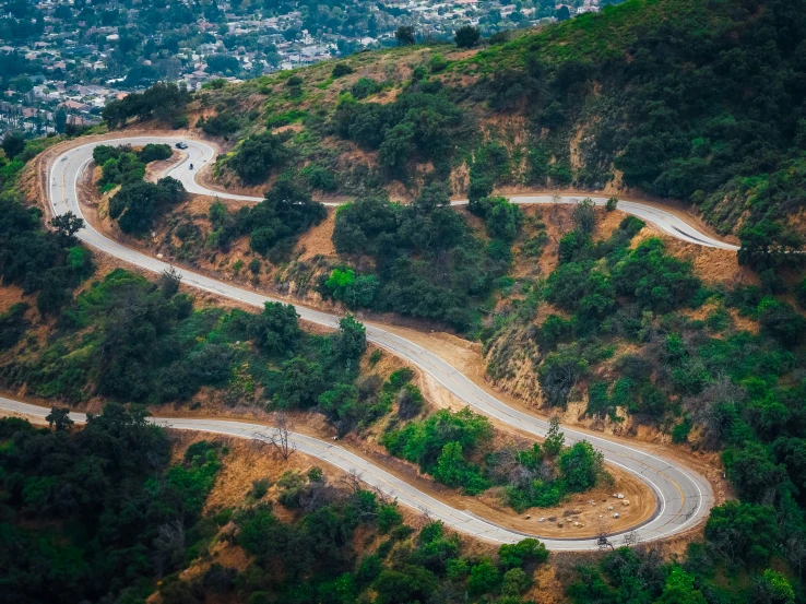 three lane road going up a hill with many trees