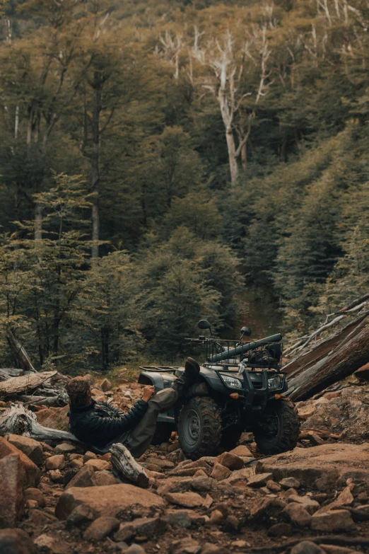 man in black shirt sitting next to an atv on rocky area