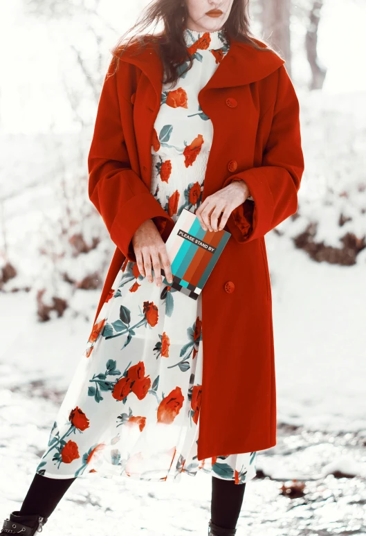 a woman in red coat and white floral print dress standing by a snowy area