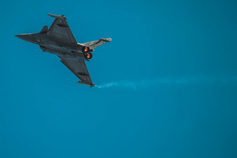 fighter jet flying through blue sky and leaving trail of smoke