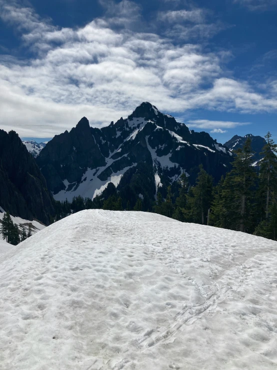 there is snow on top of a hill with mountains in the background