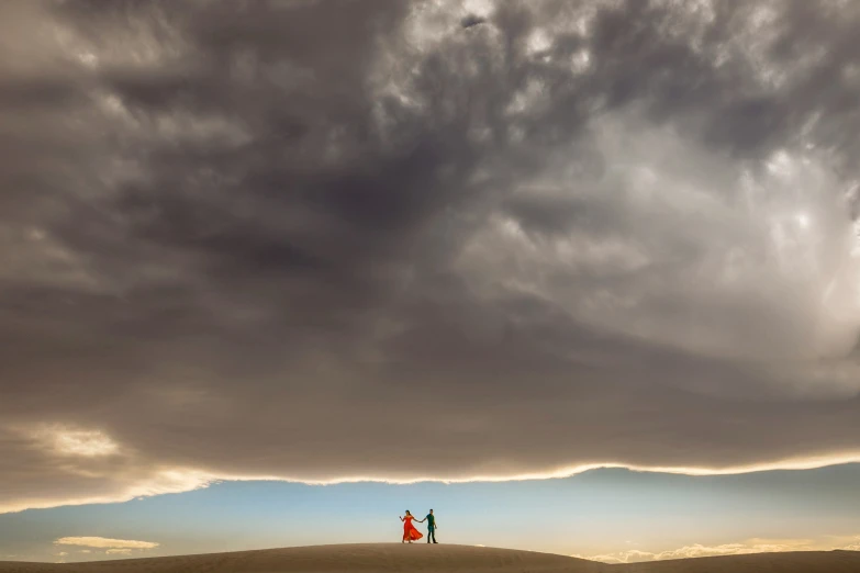 a couple is standing on a sand dune under a cloudy sky