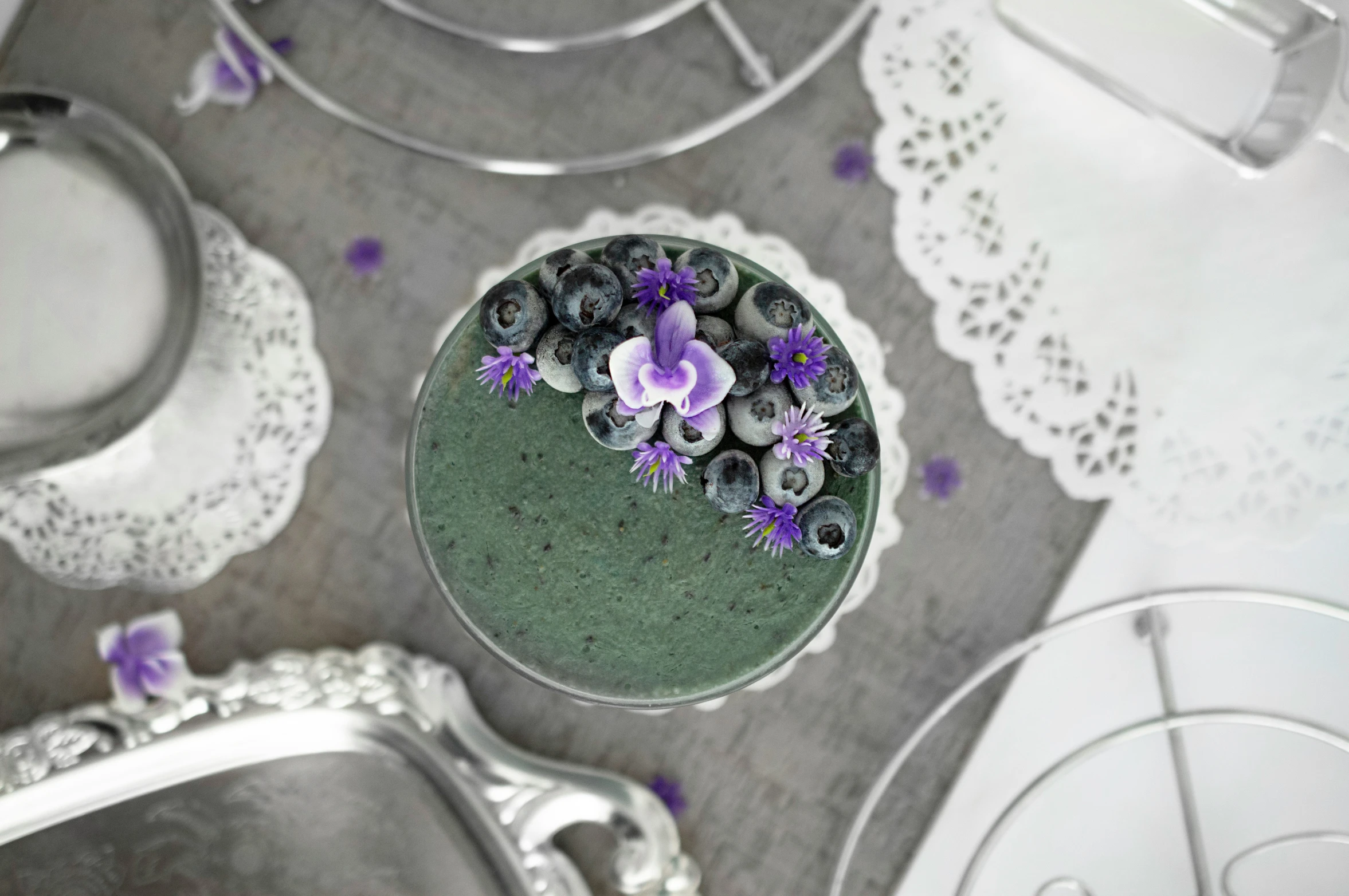 purple flowers are in the middle of silver dishes and lace doily