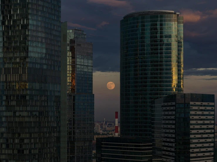 full moon with a cloudy sky behind some very tall buildings