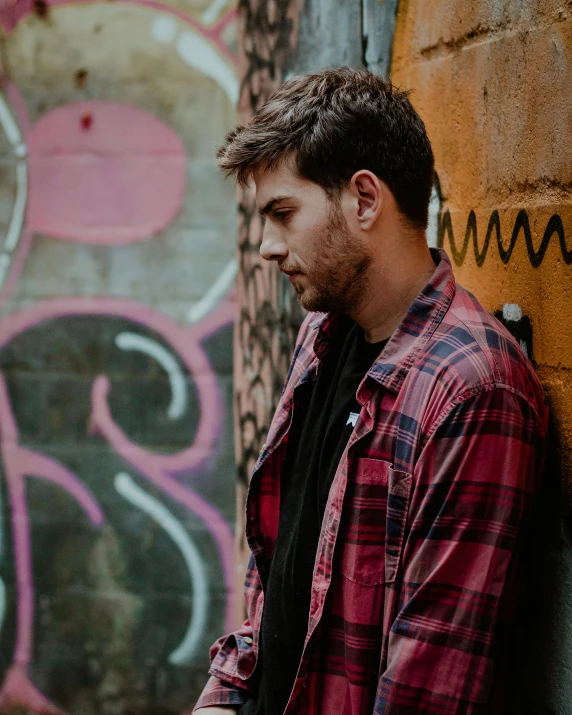 a man looking at his cell phone next to a wall covered in graffiti