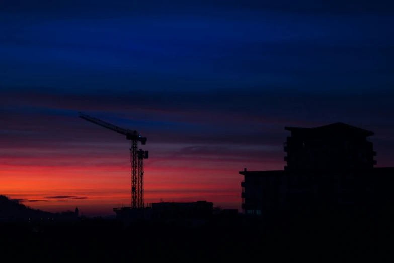 silhouettes of skyscrs with crane against cloudy sky