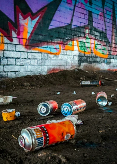 discarded soda cans are placed on the ground in front of an old graffiti wall