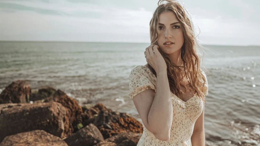 a beautiful young woman leaning up against a cliff by the ocean