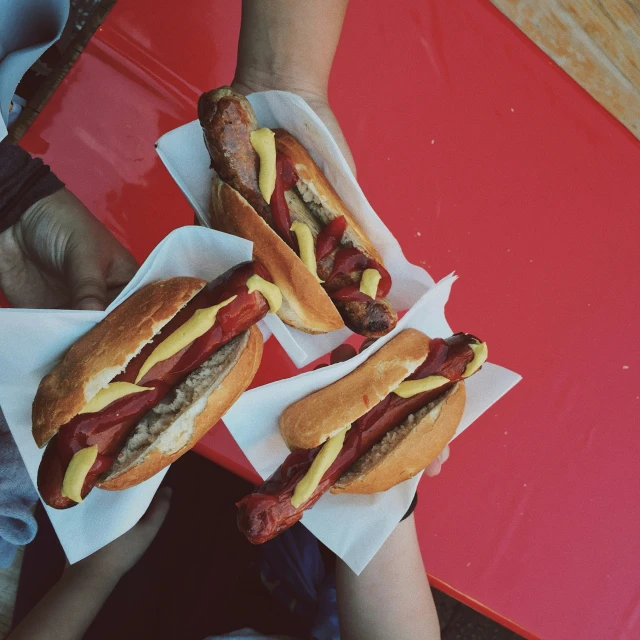 two  dogs in buns on red napkins with ketchup, mustard and relish