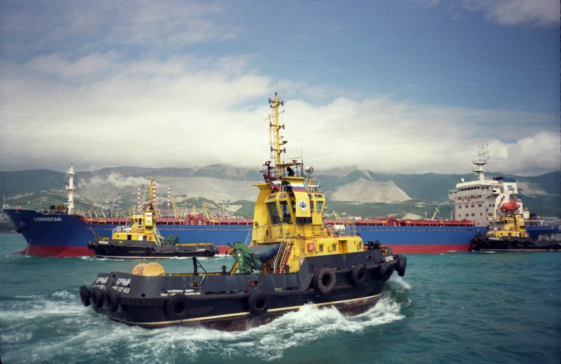 two boats pass in front of a larger ship