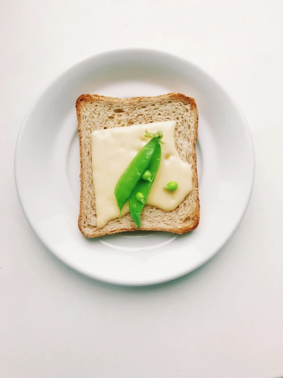 a white plate that has a piece of bread with cream and peas