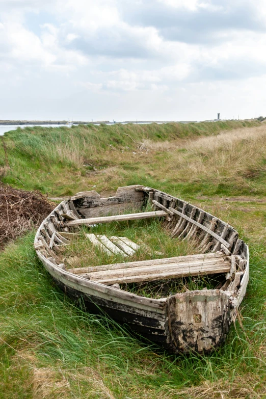 an old boat sits on the grass near a body of water