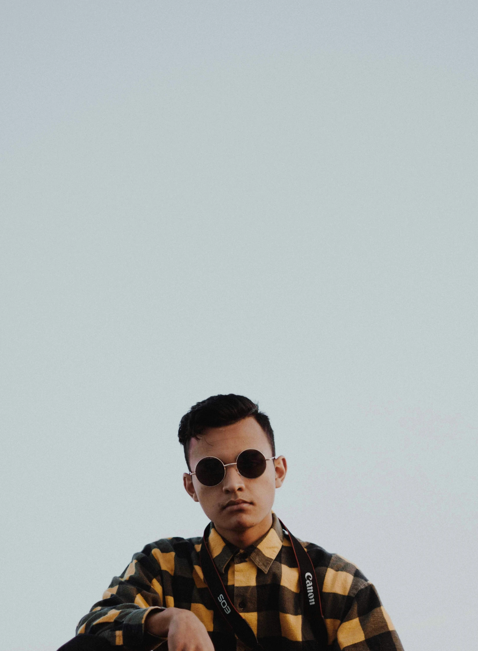 a man in sunglasses and a yellow plaid shirt looking up at the sky