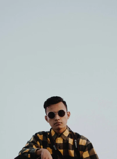a man in sunglasses and a yellow plaid shirt looking up at the sky