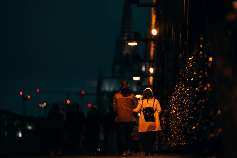 a group of people walking on the sidewalk in a city at night