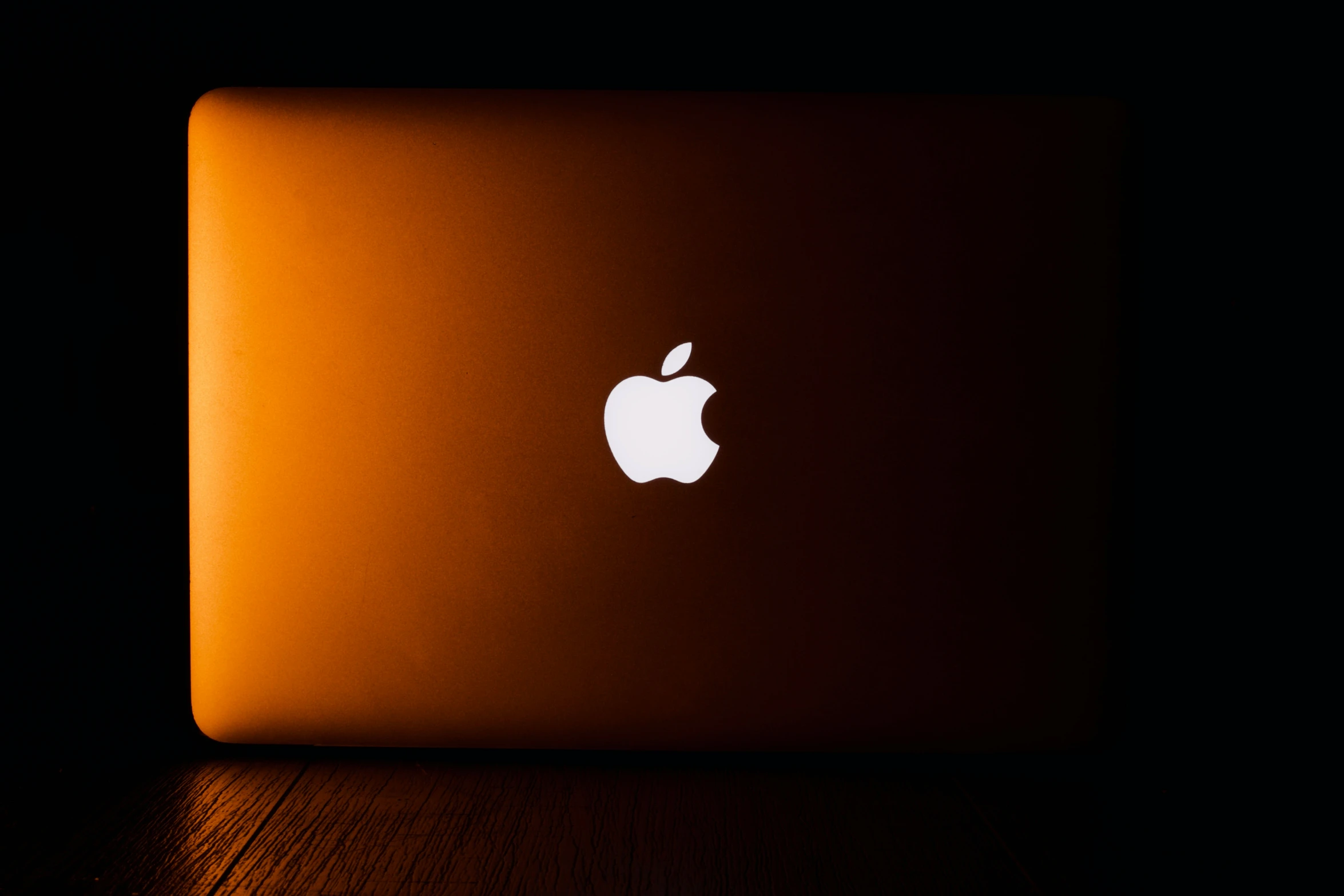 a dark room is lit by an apple laptop