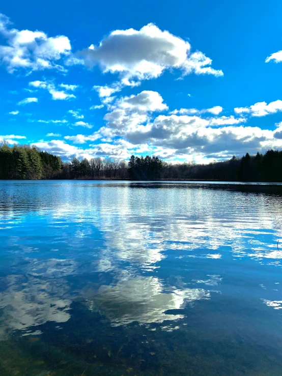 a cloudy blue sky is reflected in the calm lake