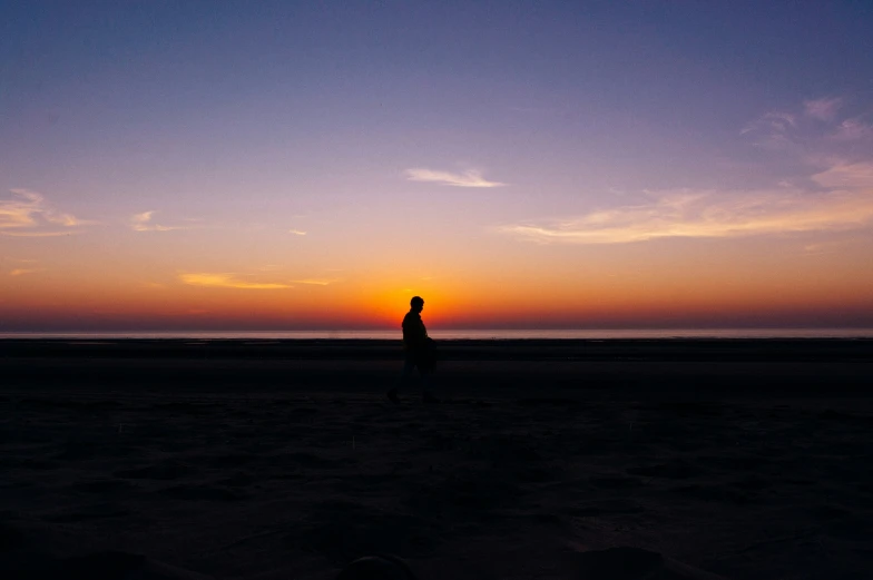 a man is standing on the beach at sunset