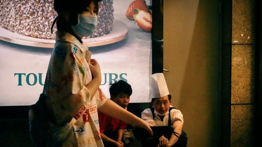 two people standing outside of a donut shop while someone in a face mask holds out their hands