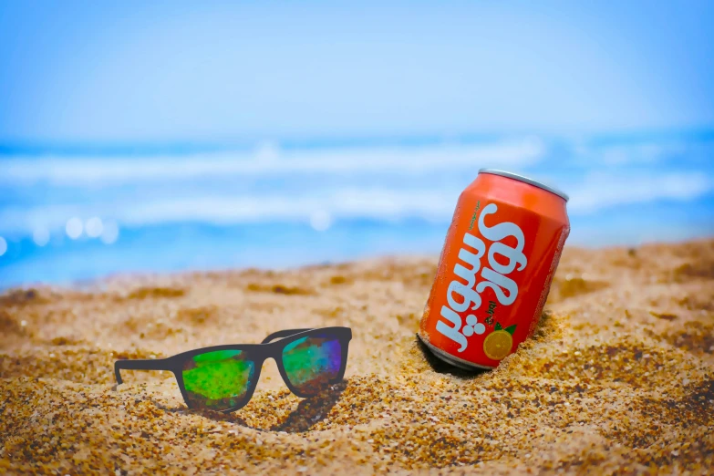 a soda can and sunglasses sitting in the sand at a beach