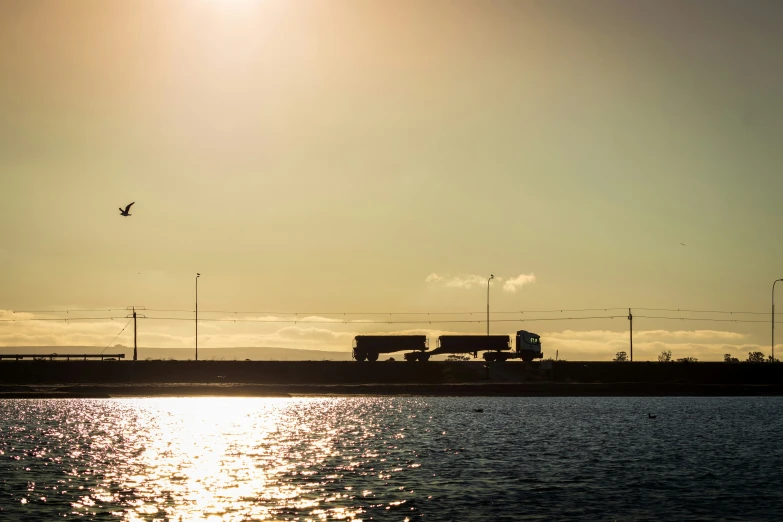 truck on highway near water with sun in background