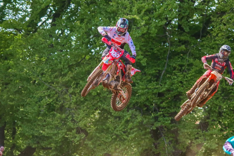 a couple of men jumping over two motorcycles on dirt