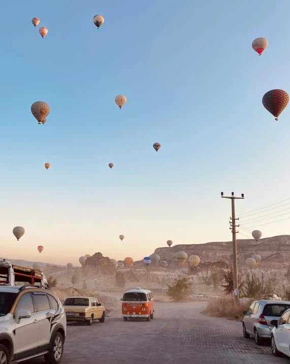 a parking lot full of cars and  air balloons in the sky