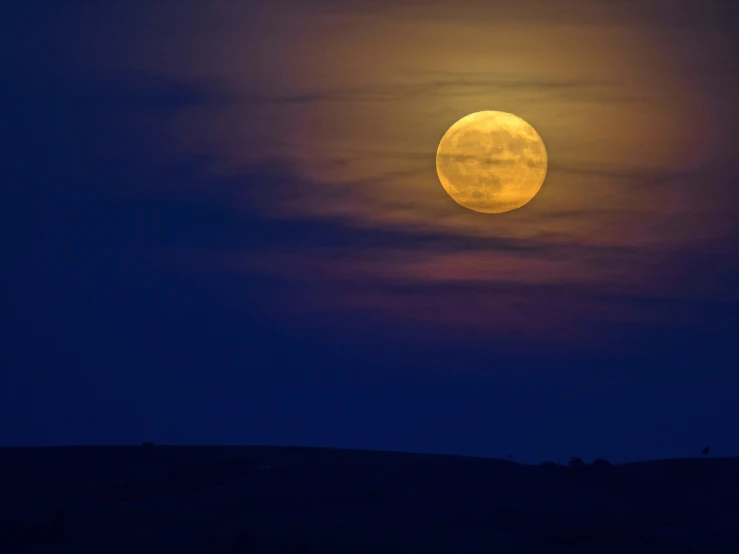 a full moon in the sky over a hill